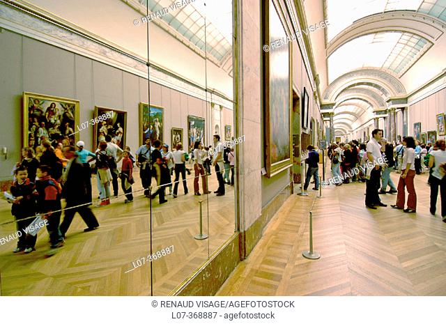Reflection of people walking along the Grand Gallery in the Denon Wing of the Louvre Museum. Paris. France