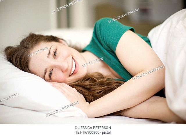 Portrait of happy young woman lying in bed