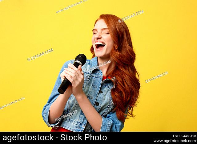 Lifestyle and People Concept: Expressive girl singing with a microphone, isolated bright yellow background