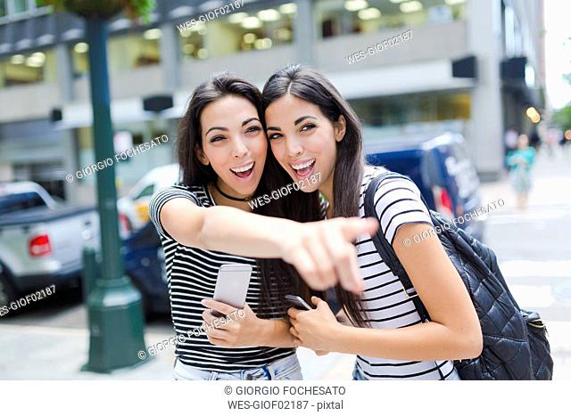 USA, New York City, two happy twin sisters with cell phones in Manhattan