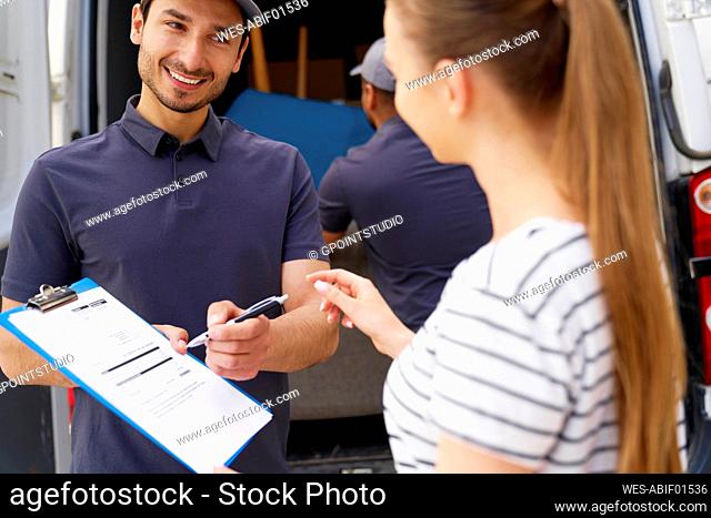 Smiling delivery man looking at female customer while passing pen to sign documents