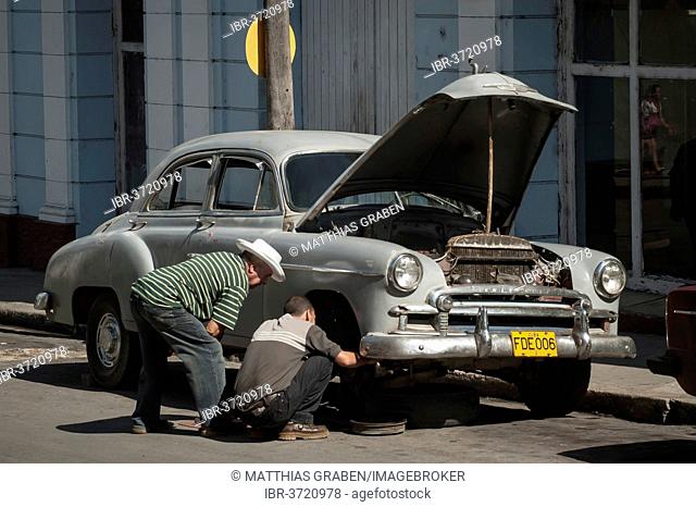 Two men repairing a vintage car in a street of Cienfuegos, Cienfuegos, Cienfuegos Province, Cuba