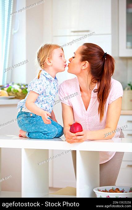 Glückliche Mutter und kleine Tochter küssen sich in der Küche