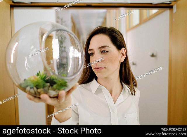Businesswoman holding terrarium in hand while standing at office