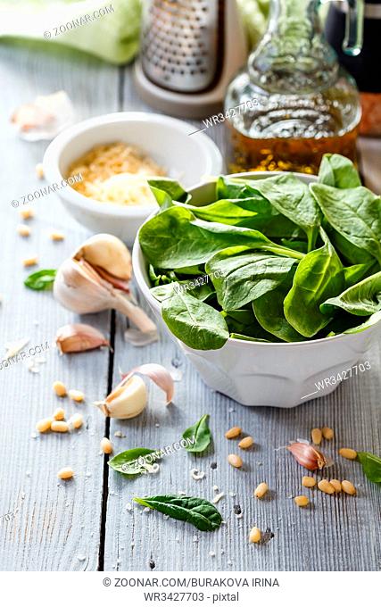Products for making homemade pesto: spinach leaves, cheese, garlic, pine nuts and olive oil on white wooden background