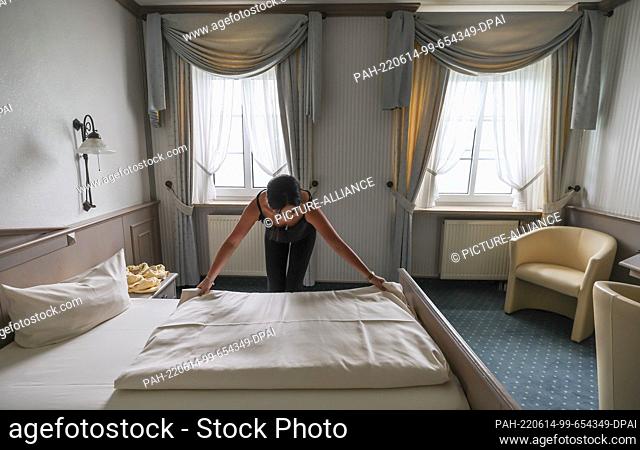 08 June 2022, Saxony, Hohenstein-Ernstthal: An employee of the Hotel Drei Schwanen smoothes a bedspread in a hotel room. After a two-year break