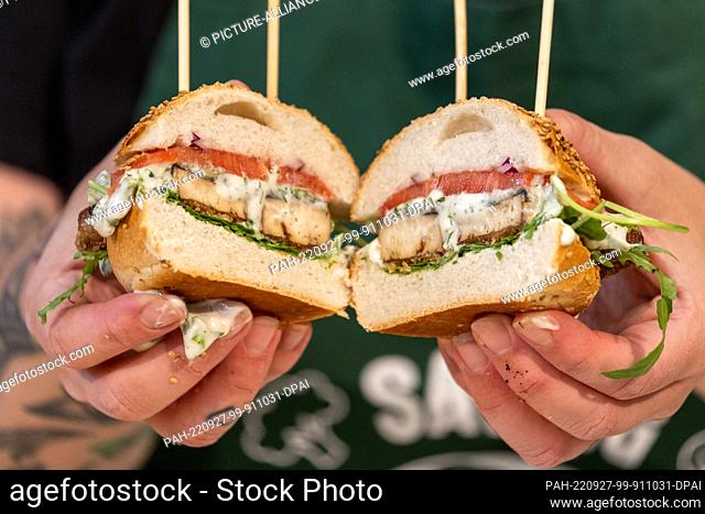 PRODUCTION - 27 July 2022, Bavaria, Nuremberg: A chef holds burgers with onions, meat tomatoes, tartar sauce and breaded fish sticks without fish