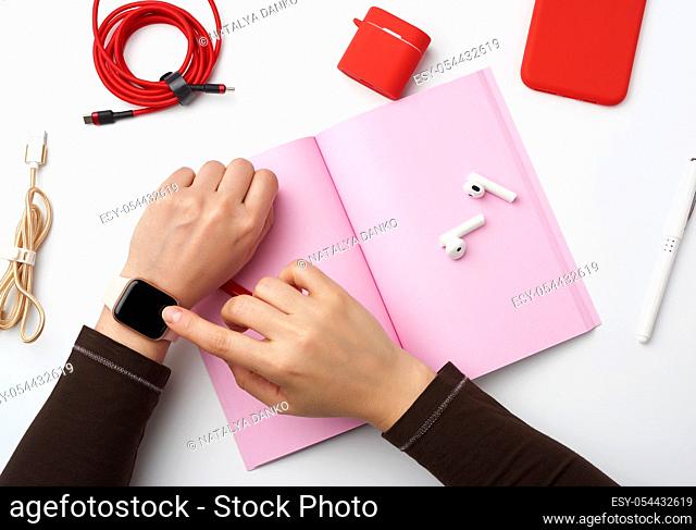 smart watch with a blank black screen is on his left hand, his right hand is touching the watch screen, a freelancerâ. . s workplace with an open notebook