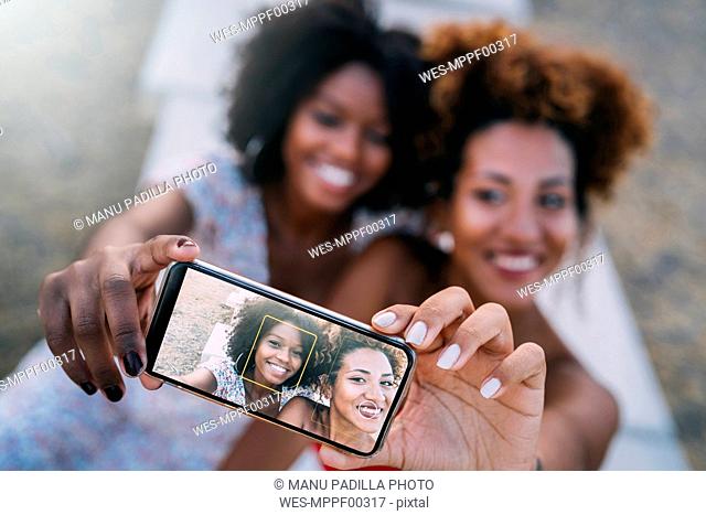 Young women smiling and making a selfie with their smart phone in a park