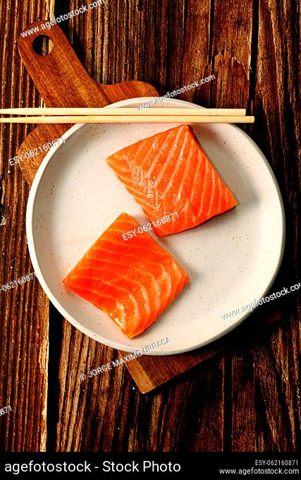 White plate with fresh and raw salmon on wooden board