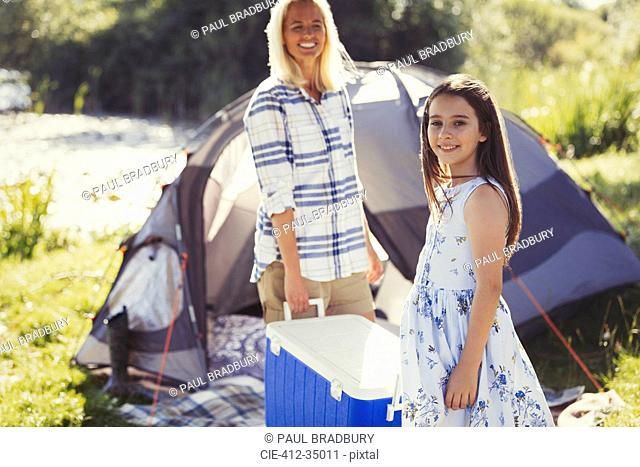 Portrait smiling mother and daughter carrying cooler outside sunny campsite tent