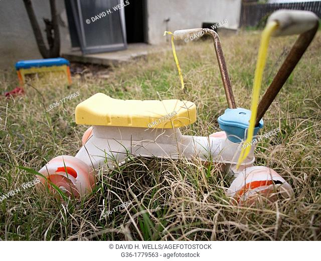 Childrens tricycle abandoned in the grass of a foreclosed home in Fresno, California, United States