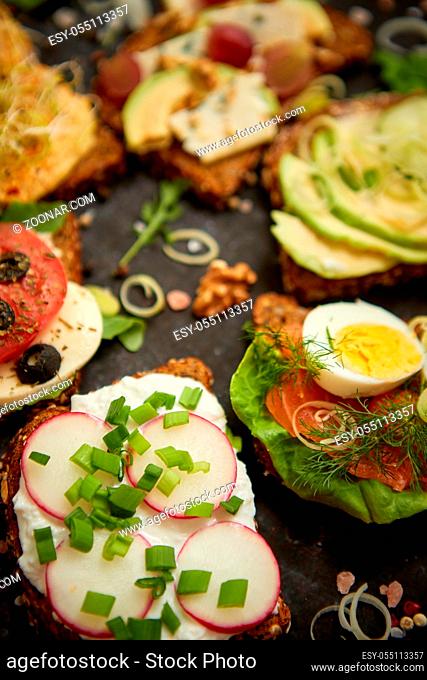 Assortment of home made sandwiches with various toppings. With colorful fresh vegetables. Healthy food concept. Top view. Black rusty background