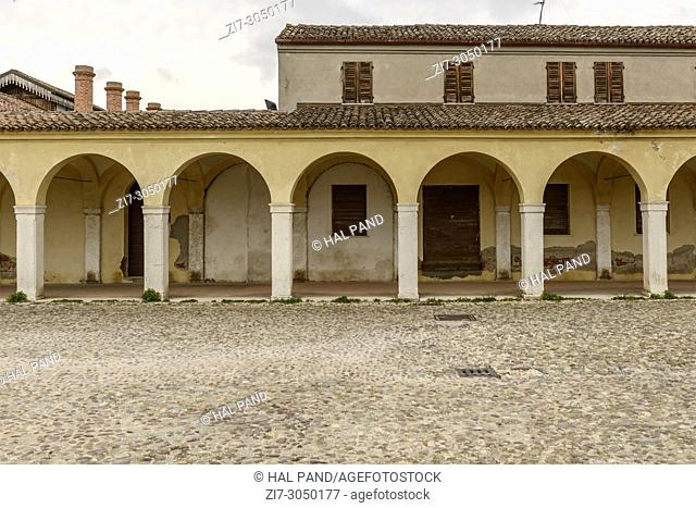 cobbled old Mazzini street in front of arches and pillars of very long Baroque santa Maria covered walkway, shot at Comacchio, Ferrara, Italy