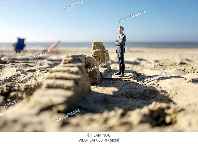 Businessman figurine standing on sand by sand buildings
