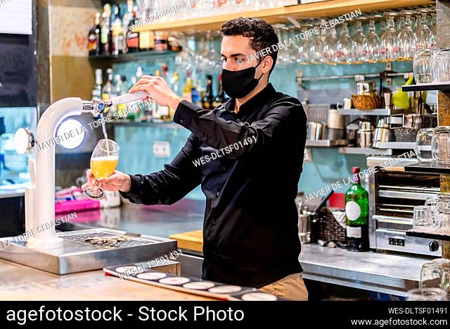 Portrait of bartender wearing protective face mask serving beer