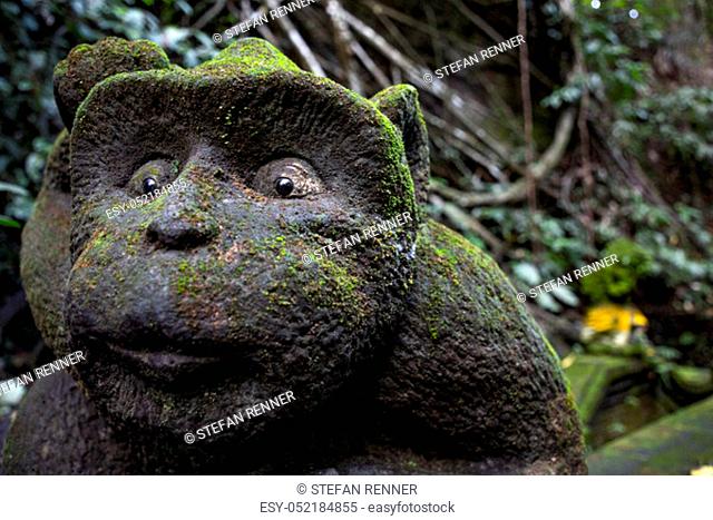 Asian stone figure overgrown by monkey with big eyes and moss