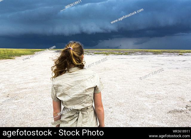 rear view of 13 year old girl looking at dramatic sky, Nxai Pan, Botswana