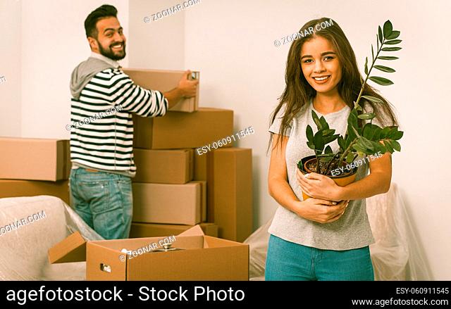 Smiling young adults moving in new home man and woman unpacking boxes standing in new apartment unpacking boxes
