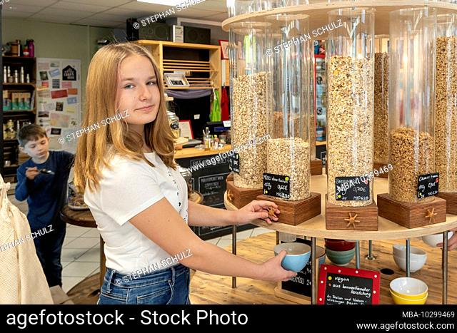A young customer stands in front of a shelf with filling containers for muesli in an unpacked shop