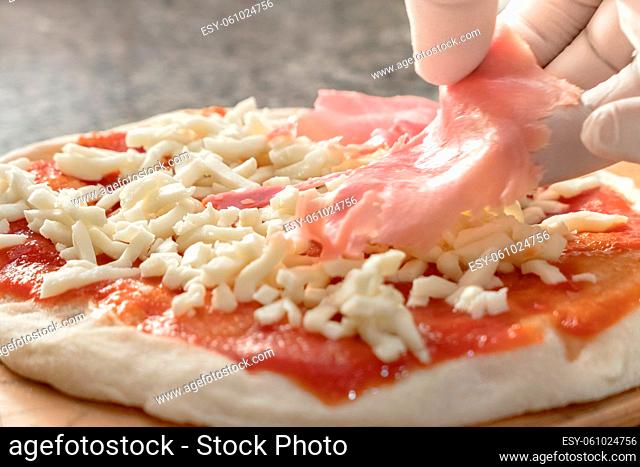 Authentic Italian delicious Pizza with Ham. Hand of pizza chef with white gloves adds cooked ham on pizza