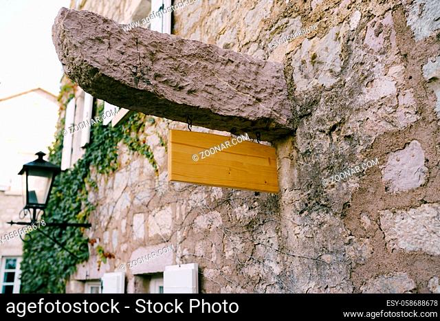 Empty wooden signboard on a stone pin of an old building amid windows, lantern and greenery. High quality photo