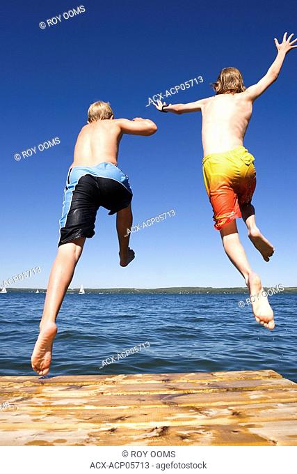 two boys 9 & 12 years old jumping off dock into lake, Sylvan Lake, Alberta, Canada