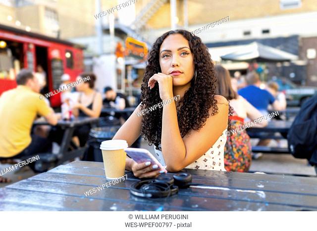 Beautiful young woman with cell phone sitting at a table and waiting