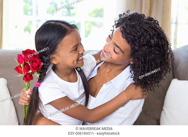 Pretty mother sitting on the couch with her daughter holding roses
