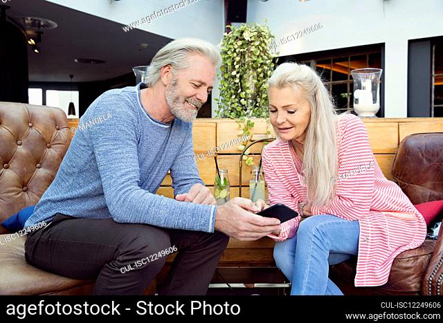 A couple sitting in a hotel reception looking at a mobile phone together