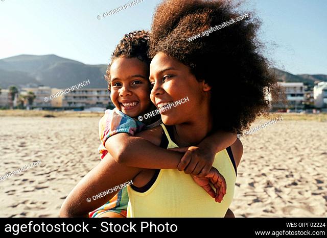 Smiling girl piggybacking sister at beach