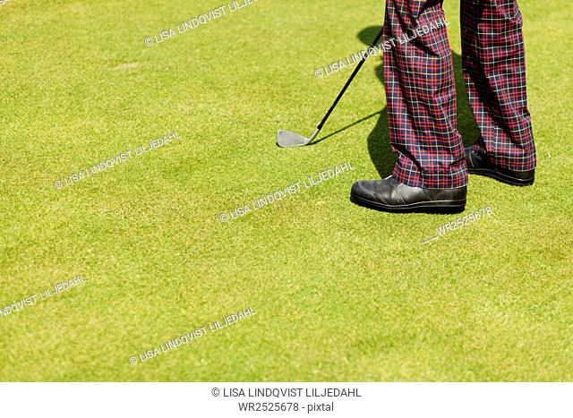 Low section of man with golf club on field