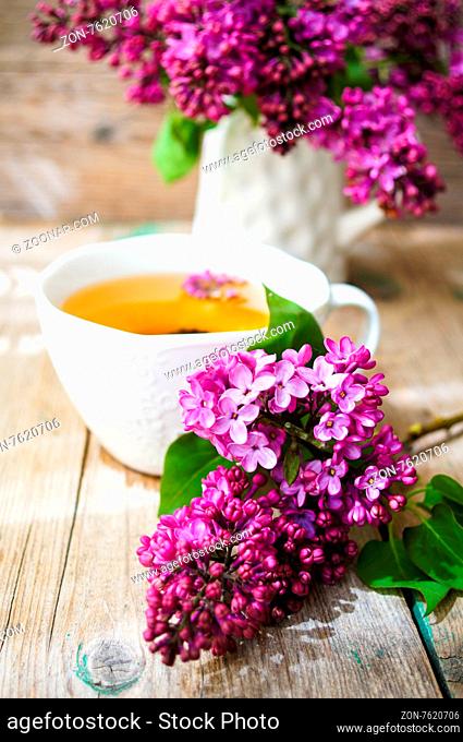 Lilac flowers in a pot and cup of tea in rustic interior