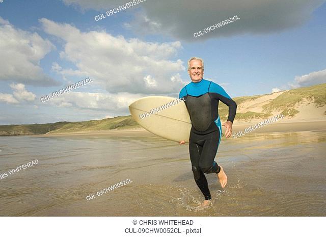 Male running into sea with a surfboard