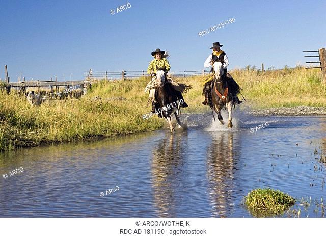 Cowboy and cowgirl in western outfit, riding through creek, Ponderosa Ranch, Oregon, USA, Wild West