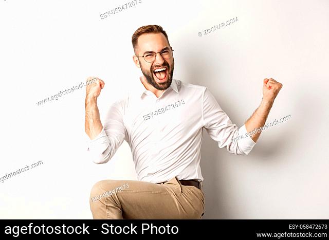 Successful businessman rejoicing, raising hands up and celebrating victory, winning something, standing over white background