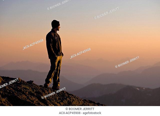 A lone mountain climber stands atop King's Peak and enjoys the last rays of the setting sun, Strathcona Park, Central Vancouver Island, British Columbia, Canada