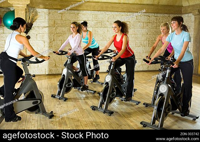 The group of women training on exercise bike at the gym with instructor
