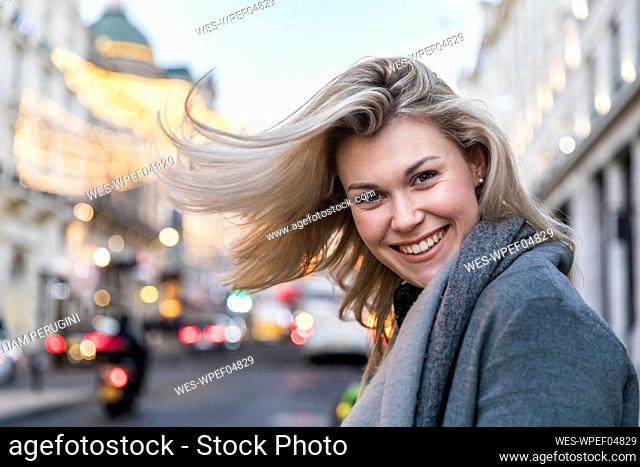 Smiling beautiful blond woman tossing hair while standing in city