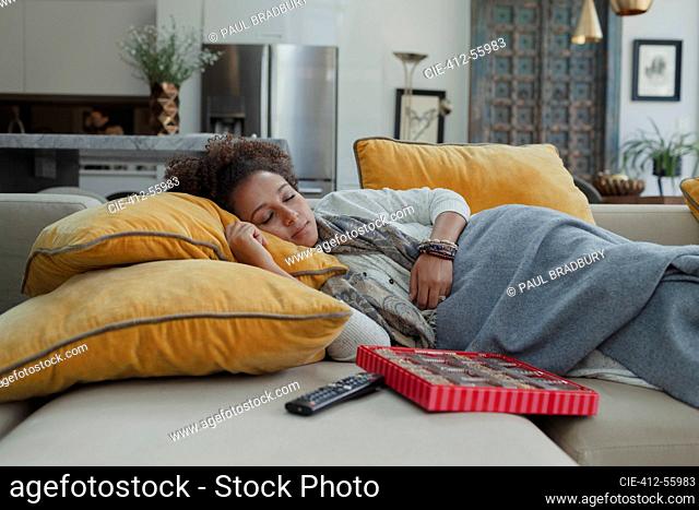 Tired woman napping on sofa next to box of chocolates