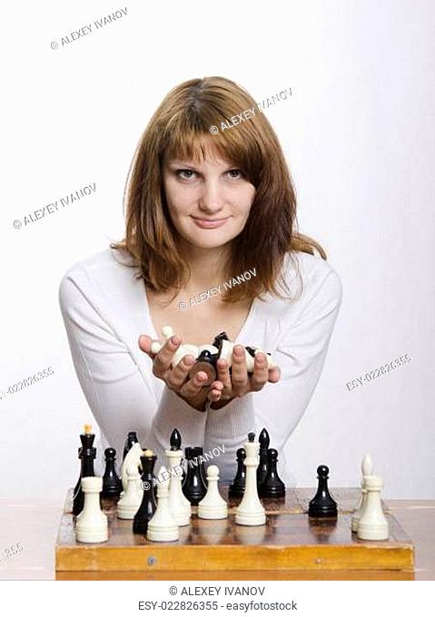 young girl with handful of figures in hands sitting at chess Board