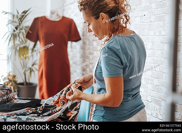 Seamstress at home workshop working with clothes in fashion industry. Professional tailor making dress. Side view of woman in hobby and leisure activity indoor...