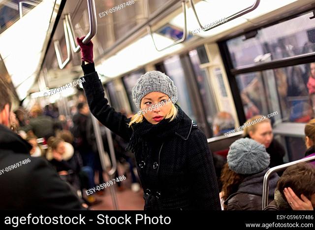 Beautiful blonde caucasian lady wearing winter coat traveling by metro in rush hour. Public transport