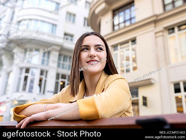 Smiling young woman with brown hair looking away in front of building