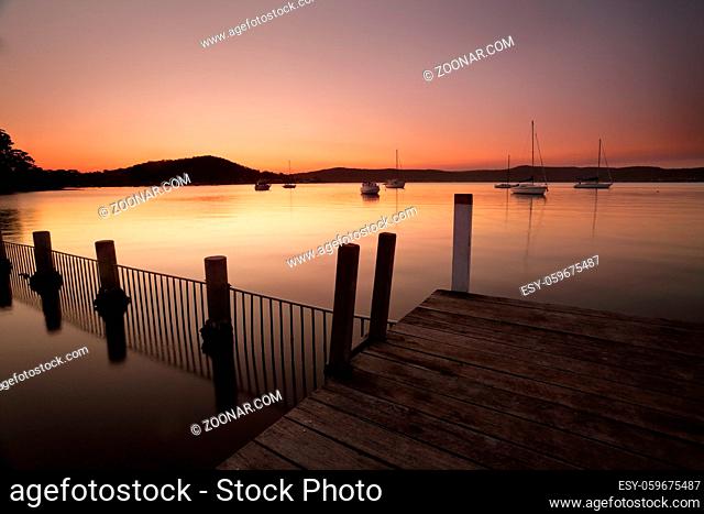 Dusk colours of orange pink and purple fill the sky and reflect in the waterfront of Yattalunga on the Central Coast of Australia