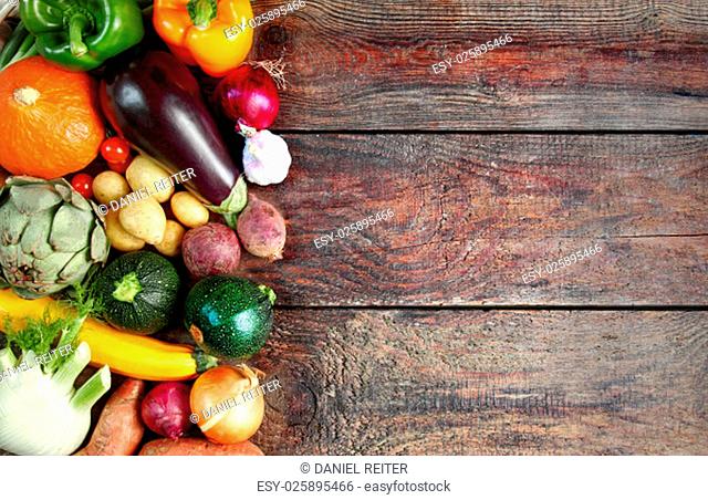 Selection of fresh autumn vegetables in a border to the left side of the frame over a rustic wooden background with copyspace, overhead view