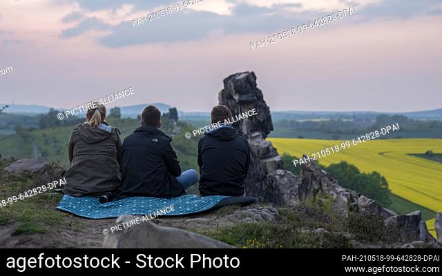 14 May 2021, Saxony-Anhalt, Thale: Three young people enjoy the sunset at the Teufelsmauer (Devil's Wall) in the Harz mountains: the rugged landscape is part of...
