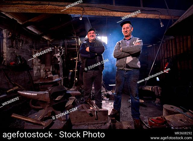 portrait of two generations confident blacksmith standing with crossed arms in the traditional workshop