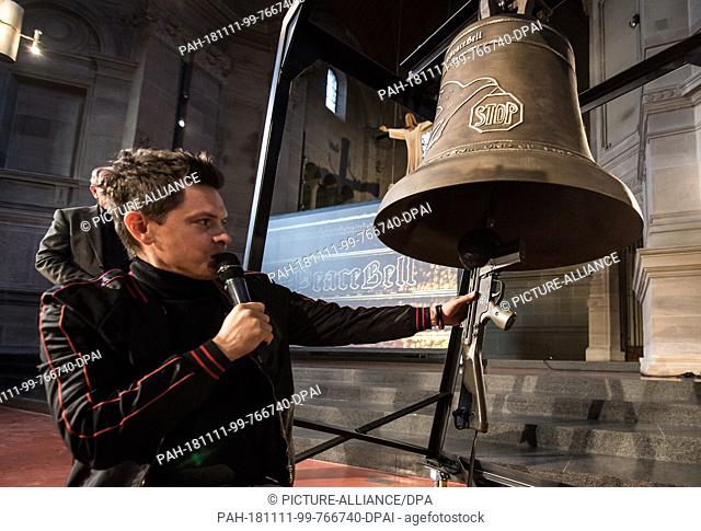 11 November 2018, Rhineland-Palatinate, Mainz: The Irish-American singer Michael Patrick Kelly kneels next to the peace bell in the Christuskirche Mainz and...