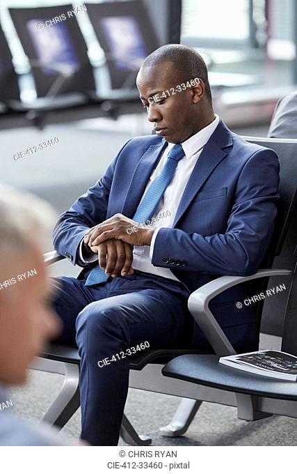 Businessman checking the time on wristwatch waiting in airport departure area